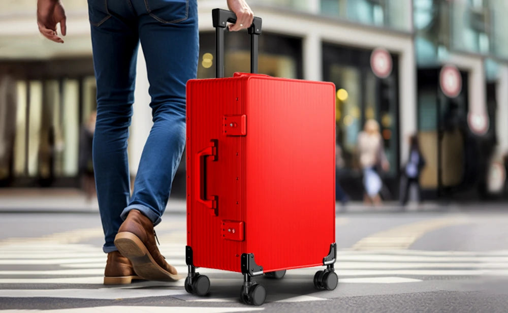 Person in blue jeans walking confidently with a red Hexter +Plus Aluminium Luggage on wheels, suggesting stylish and convenient travel through an urban setting.